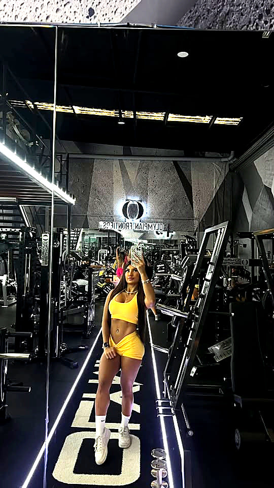 A customer wearing the SYNQ Sports Bra and Sculpt Shorts in Solar Yellow at the gym